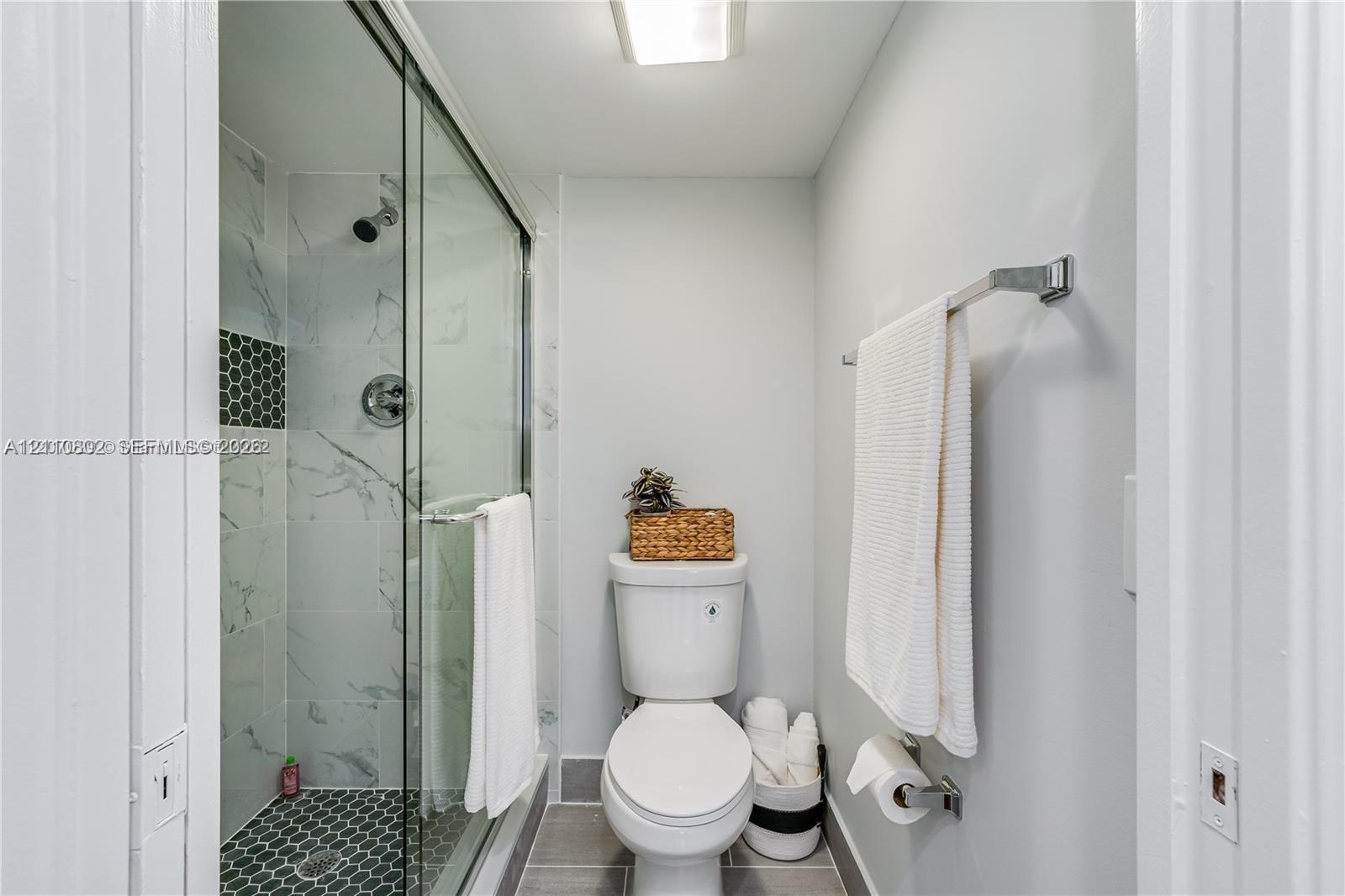 Walk-in shower with glass enclosure, large-format tile wall surround, geometric floor tiling, and a metal towel rack