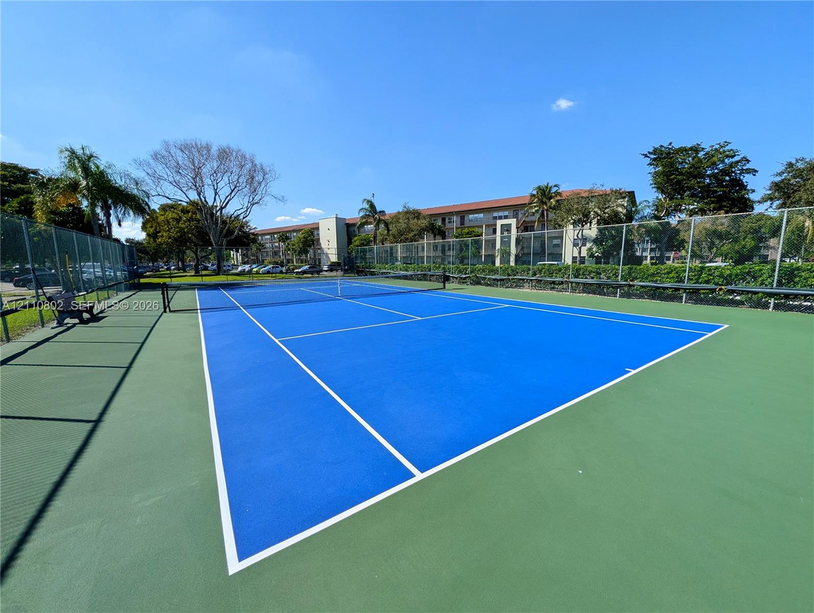 Tennis court featuring a high-contrast blue and green surface, permanent net, and perimeter chain-link fencing
