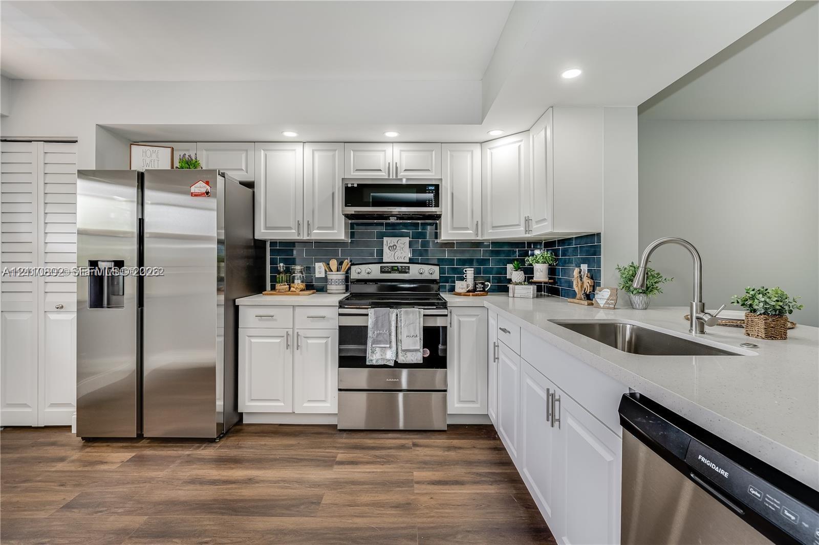 Kitchen featuring white shaker-style cabinetry, stainless steel appliances, dark subway-tile backsplash, stone-finish countertops, and wood-finish flooring Kitchen featuring white shaker-style cabinetry, stainless steel appliances, dark subway-tile backsplash, stone-finish countertops, and wood-finish flooring
