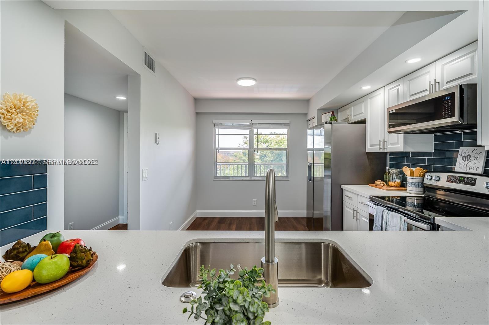 Kitchen featuring a quartz countertop, stainless steel under-mount sink, white shaker-style cabinetry, dark tiled backsplash, and wood-finish flooring Kitchen featuring a quartz countertop, stainless steel under-mount sink, white shaker-style cabinetry, dark tiled backsplash, and wood-finish flooring