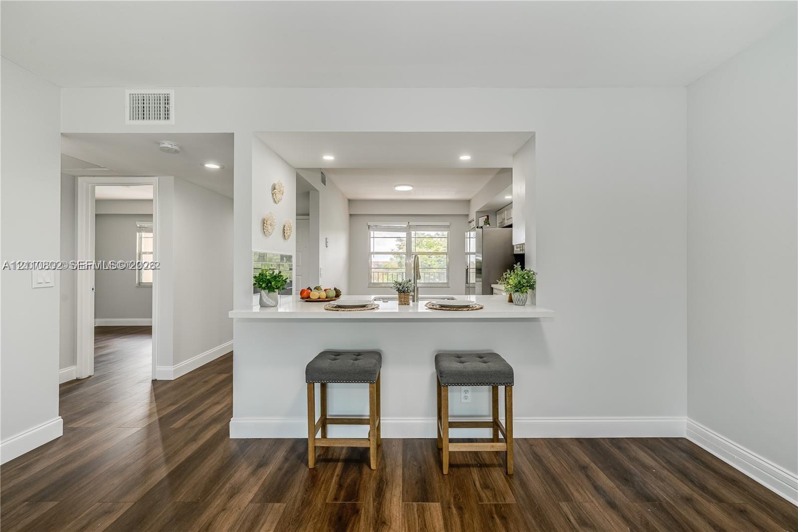 Kitchen featuring an open pass-through window with a quartz countertop breakfast bar, recessed lighting, and wood-finish flooring Kitchen featuring an open pass-through window with a quartz countertop breakfast bar, recessed lighting, and wood-finish flooring