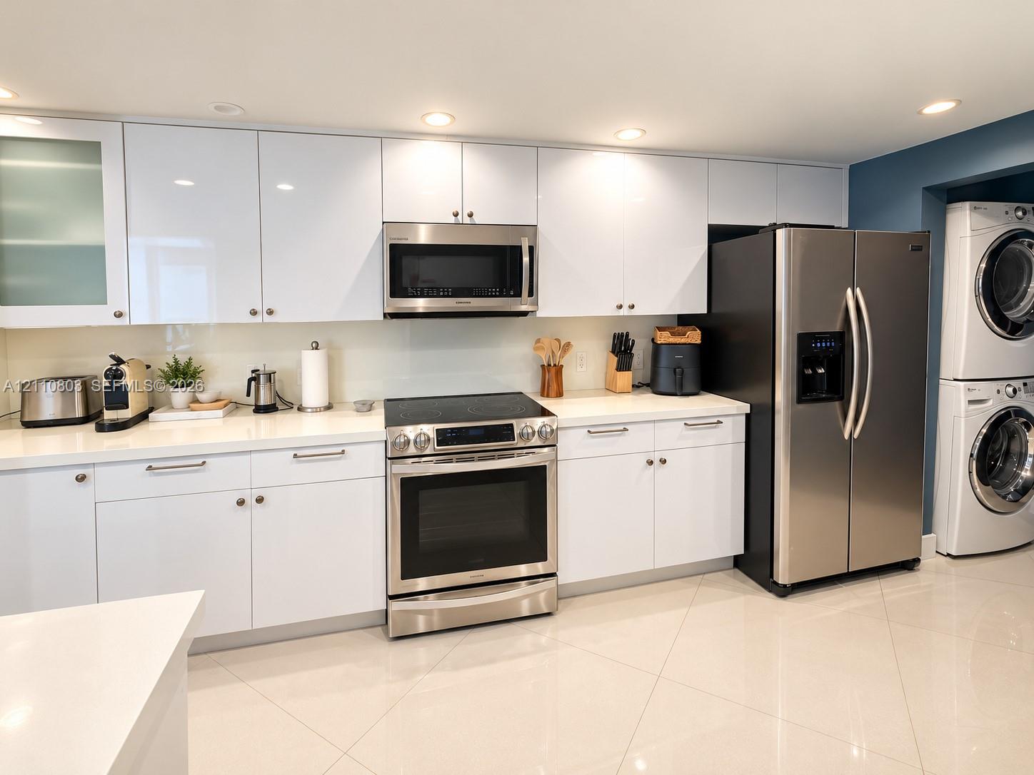 Contemporary kitchen featuring high-gloss white cabinetry, solid-surface countertops, stainless steel appliances, and large-format tile flooring, complete with a built-in laundry station