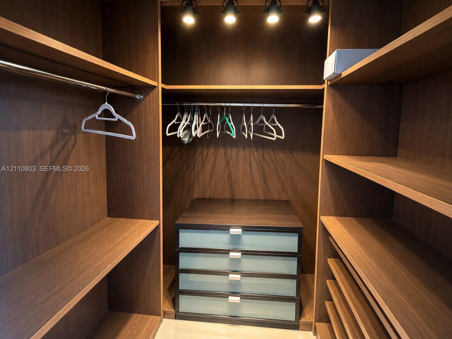 Custom closet cabinetry featuring dark wood-finish shelving, integrated hanging rods, a built-in four-drawer dresser with frosted glass fronts, and overhead directional track lighting
