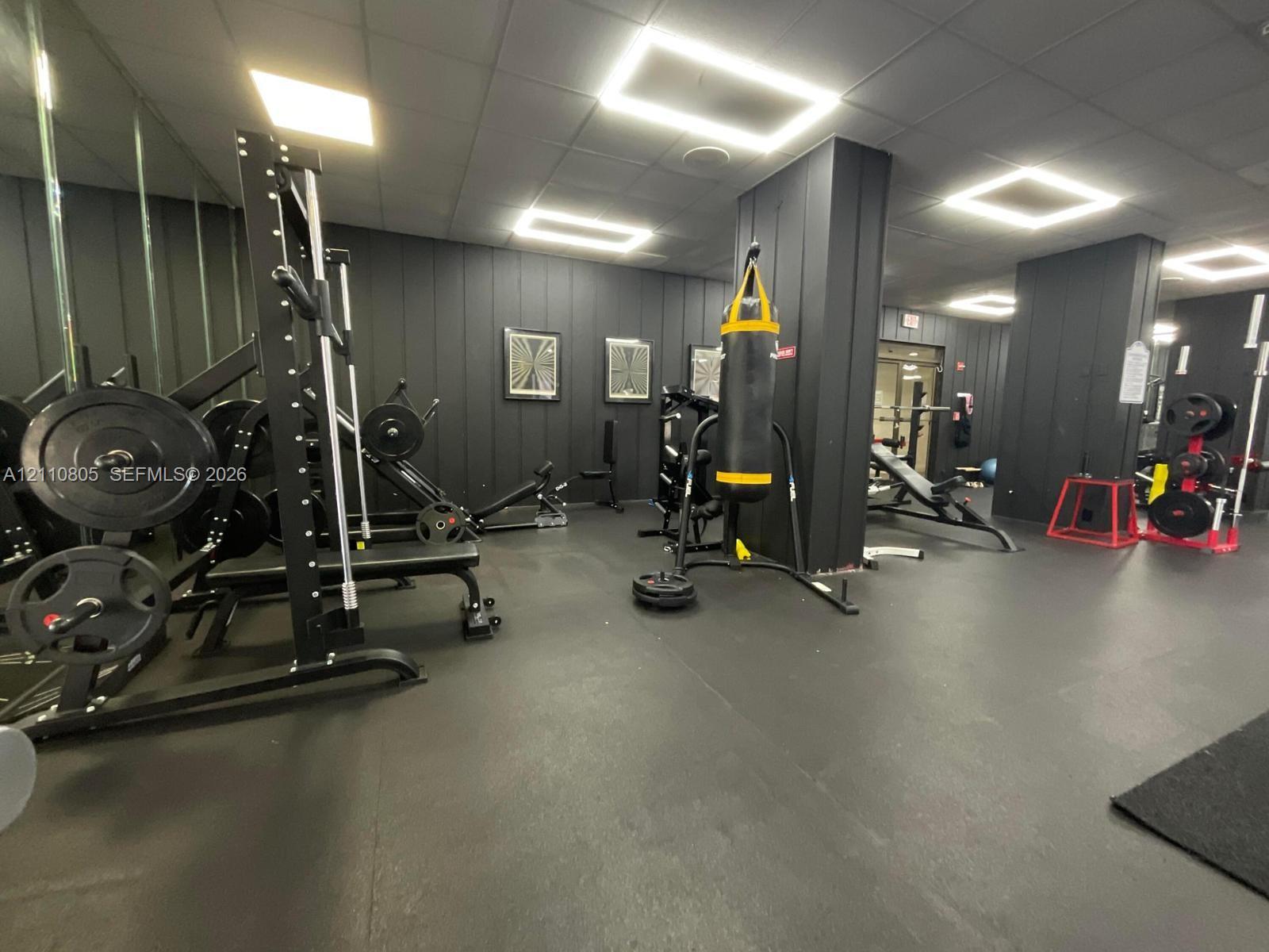 Fitness space featuring matte black vertical paneling, recessed square LED lighting, floor-to-ceiling mirrored walls, and durable rubberized flooring