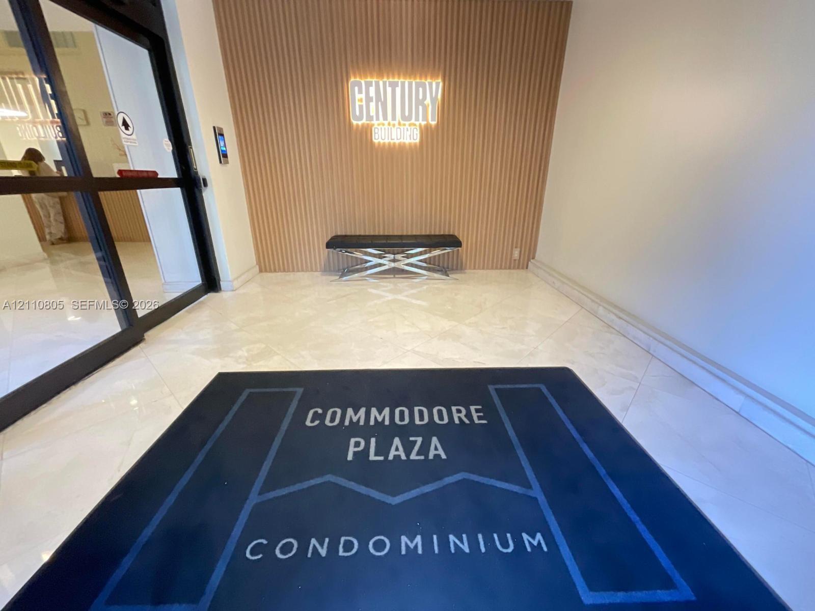 Building entrance lobby featuring polished stone flooring, vertical slat wood-finish wall paneling, and illuminated signage
