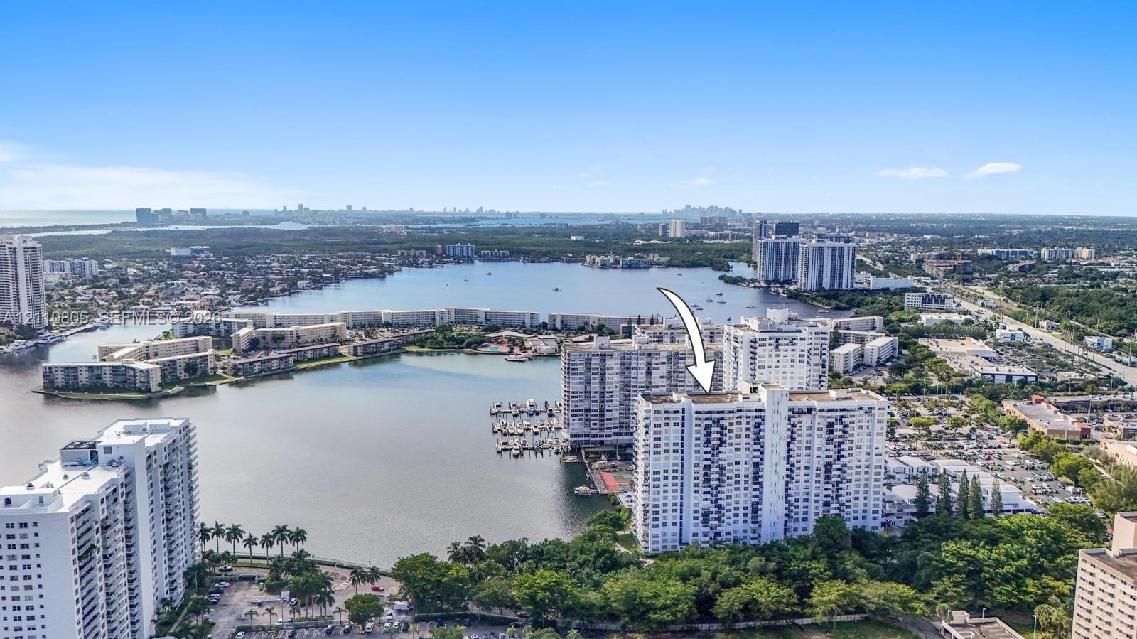 Aerial perspective of high-rise building situated on a peninsula, featuring immediate water frontage, deep-water marina, and tropical landscaping