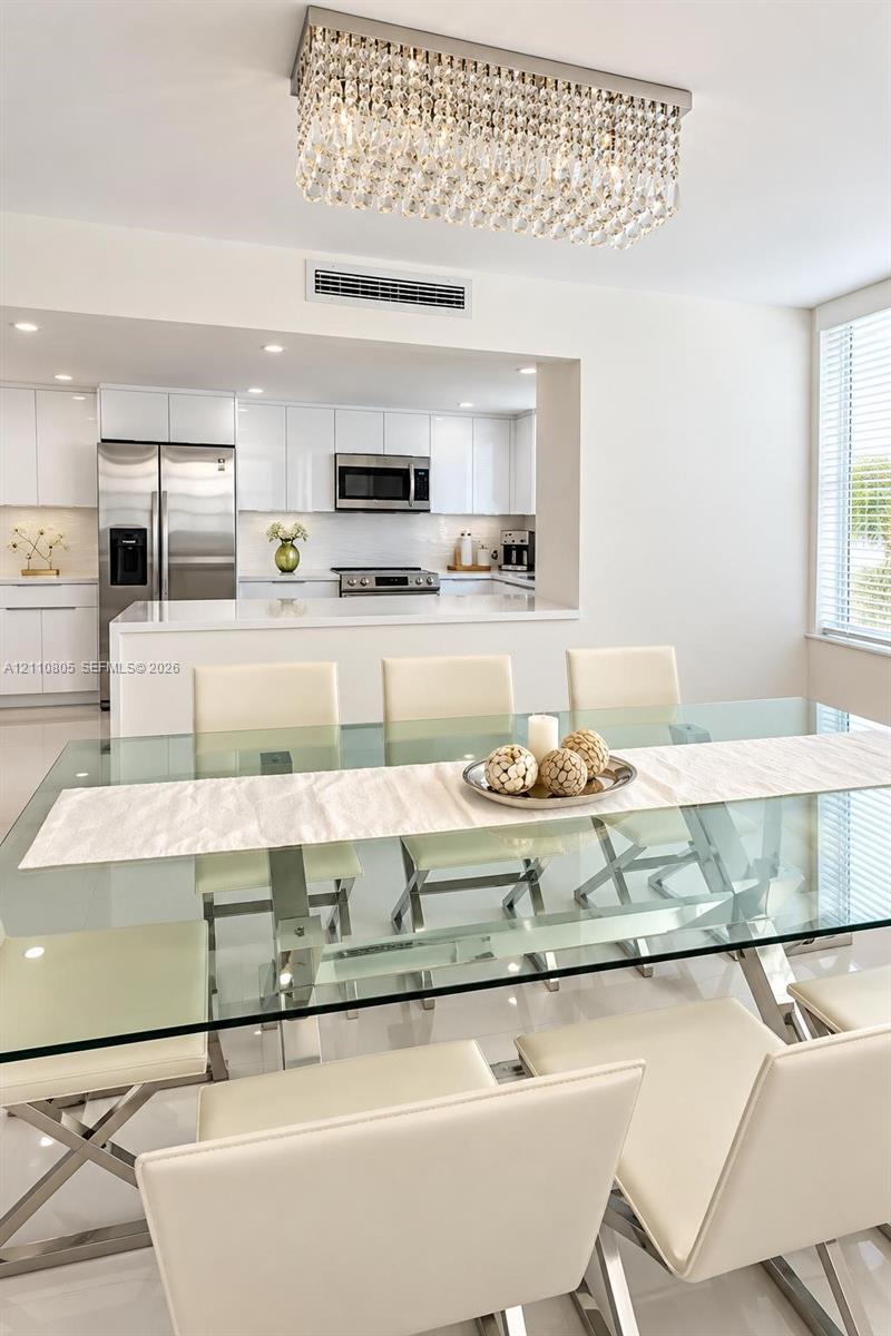 Modern dining area featuring a tiered crystal chandelier, glossy tile flooring, and clean-lined cabinetry in the kitchen Modern dining area featuring a tiered crystal chandelier, glossy tile flooring, and clean-lined cabinetry in the kitchen