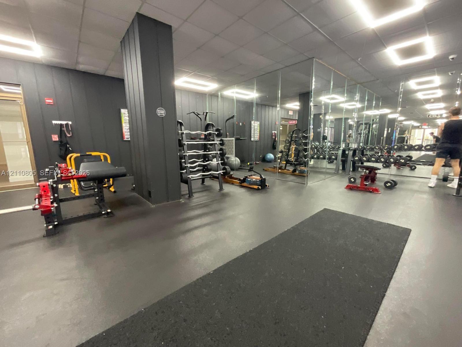 Fitness center featuring dark vertical paneled walls, mirrored wall sections, recessed square ceiling lighting, and smooth industrial-style flooring