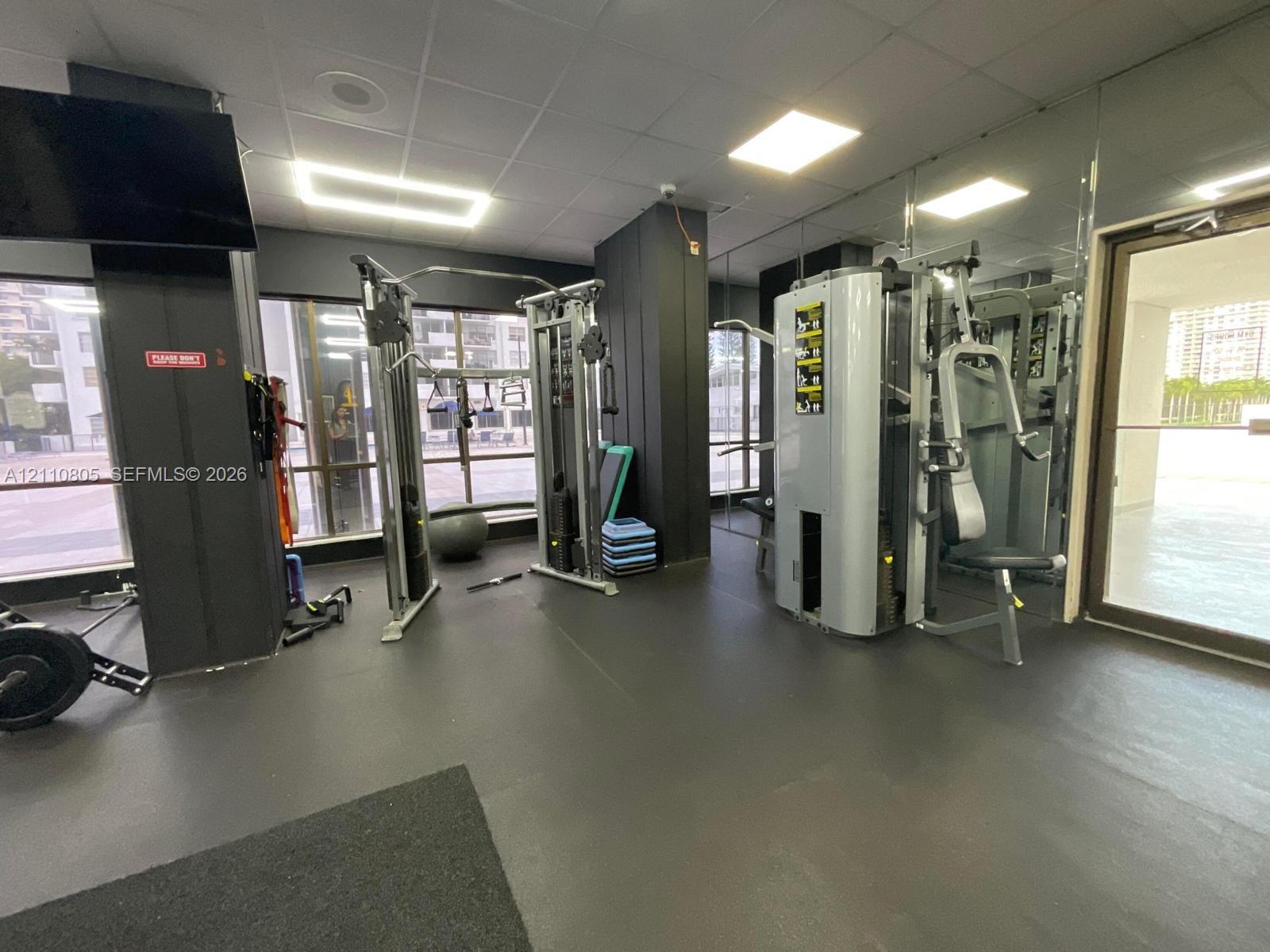 Fitness room featuring floor-to-ceiling mirror wall, rubberized flooring, recessed square lighting, and large windows