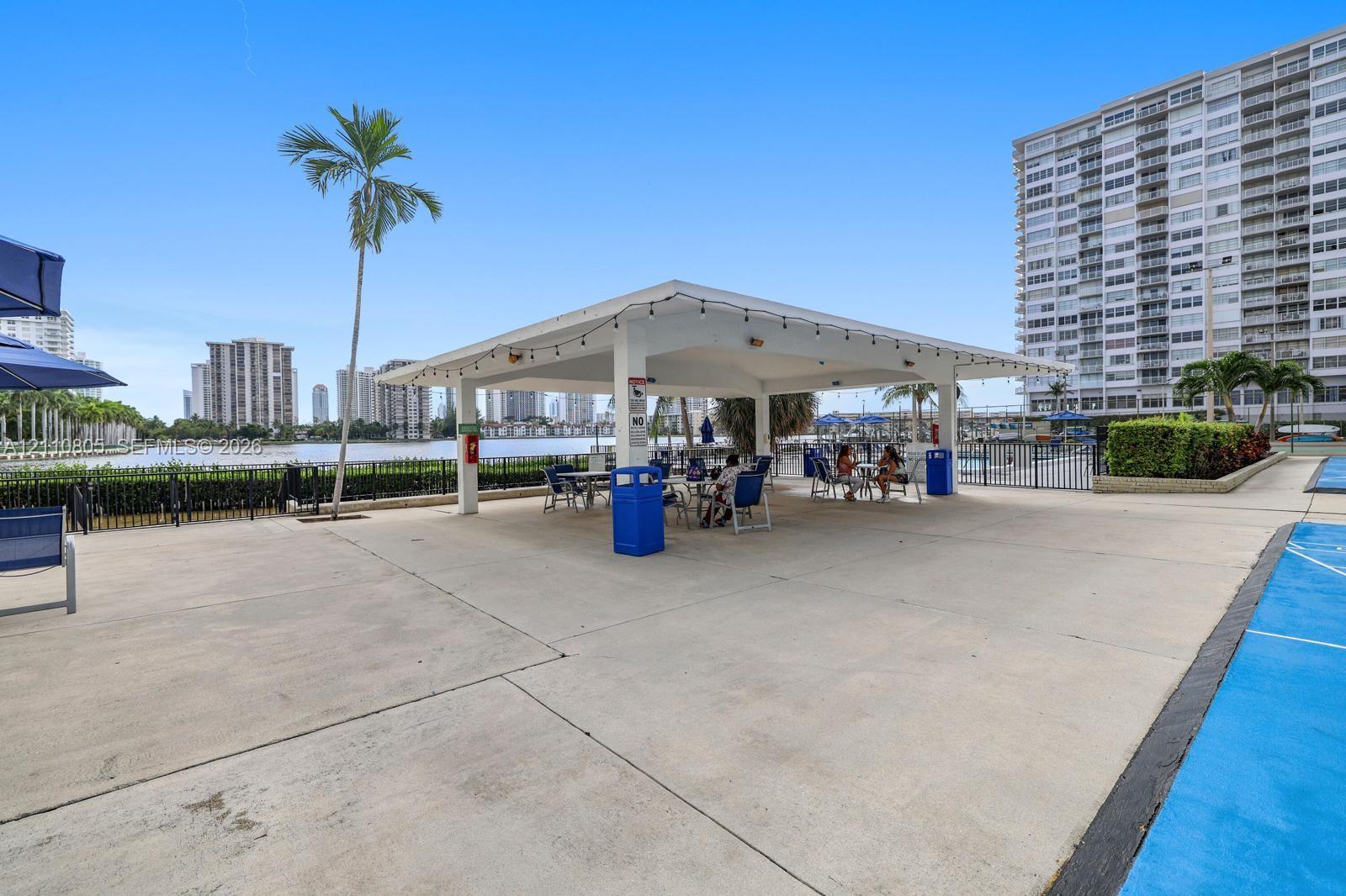 Covered outdoor pavilion featuring a concrete patio, perimeter metal fencing, and water frontage