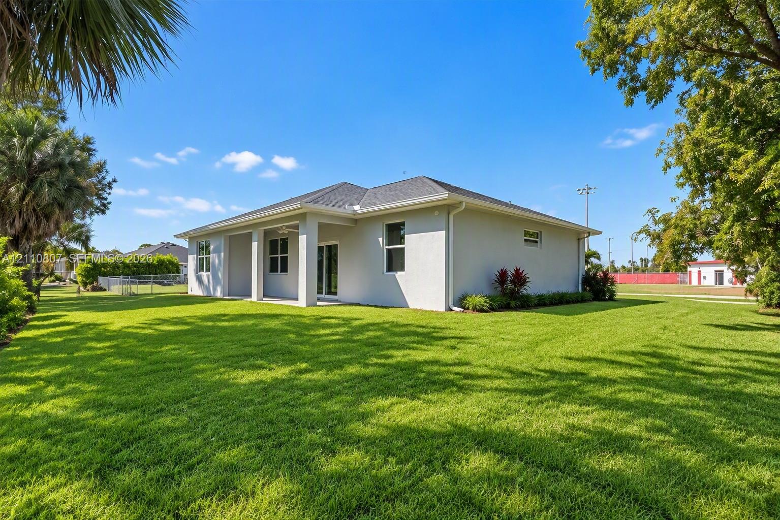 Exterior of the home featuring a light-colored stucco finish, a hip roof, a covered patio, and an expansive lawn with mature landscaping