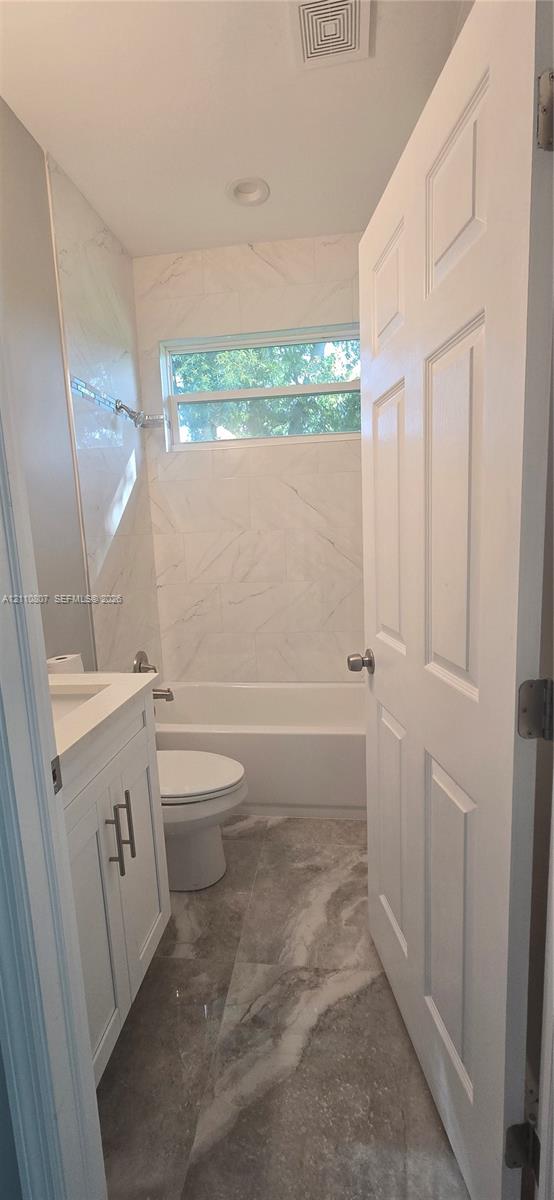 Bathroom featuring large-format tile flooring, a white vanity with metallic hardware, and a tub-shower combination with full-height wall tiling