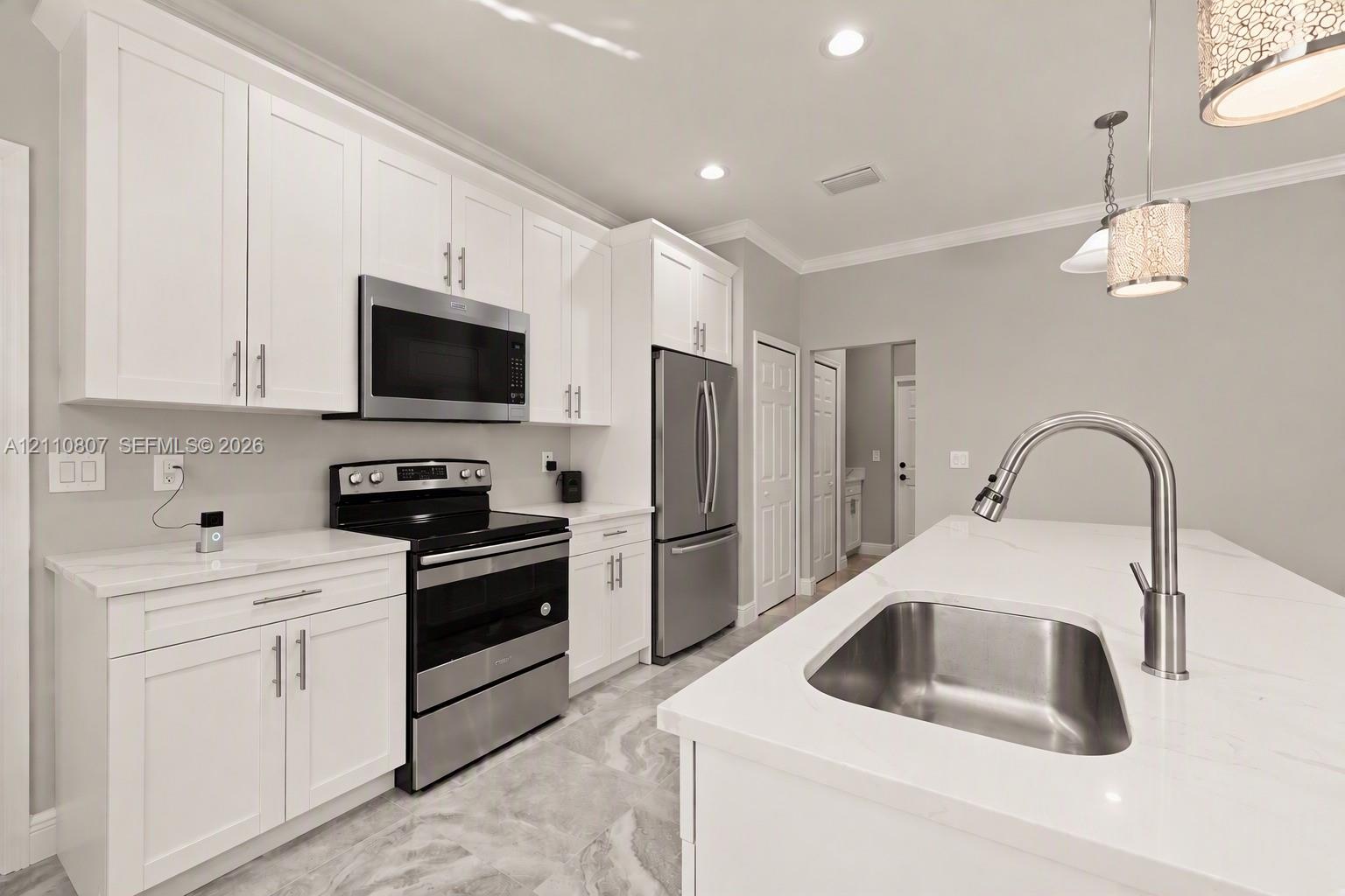 Kitchen featuring white shaker-style cabinetry, quartz countertops, stainless steel appliances, a central island with an undermount sink, and stone-finish tile flooring