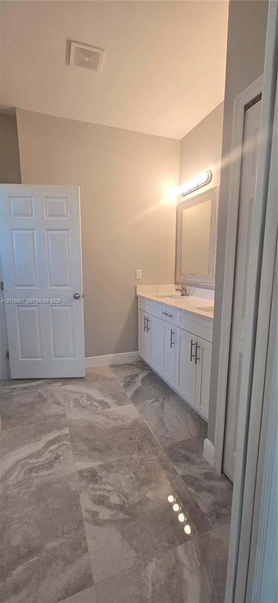 White vanity cabinet featuring brushed nickel hardware, light-toned countertop with integrated sink, framed wall mirror, and large-format porcelain tile flooring