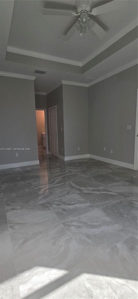 Tray ceiling with crown molding, polished large-format tile flooring, and a ceiling fan