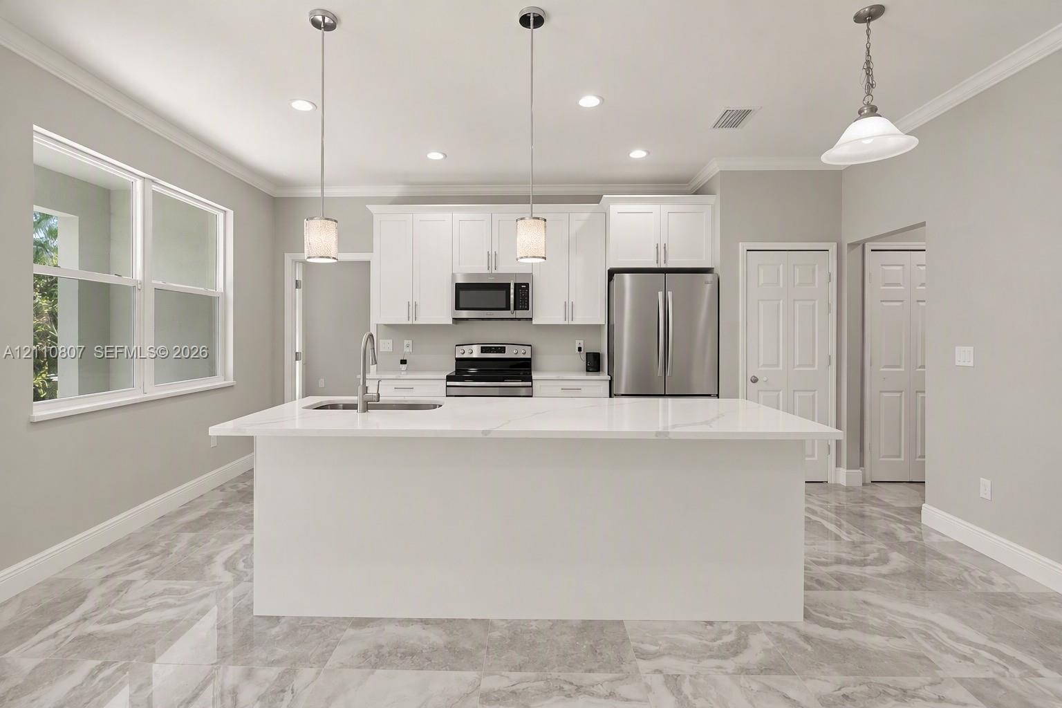 Kitchen featuring white shaker-style cabinetry, quartz countertops, a central island with an integrated sink, stainless steel appliances, and large-format porcelain tile flooring