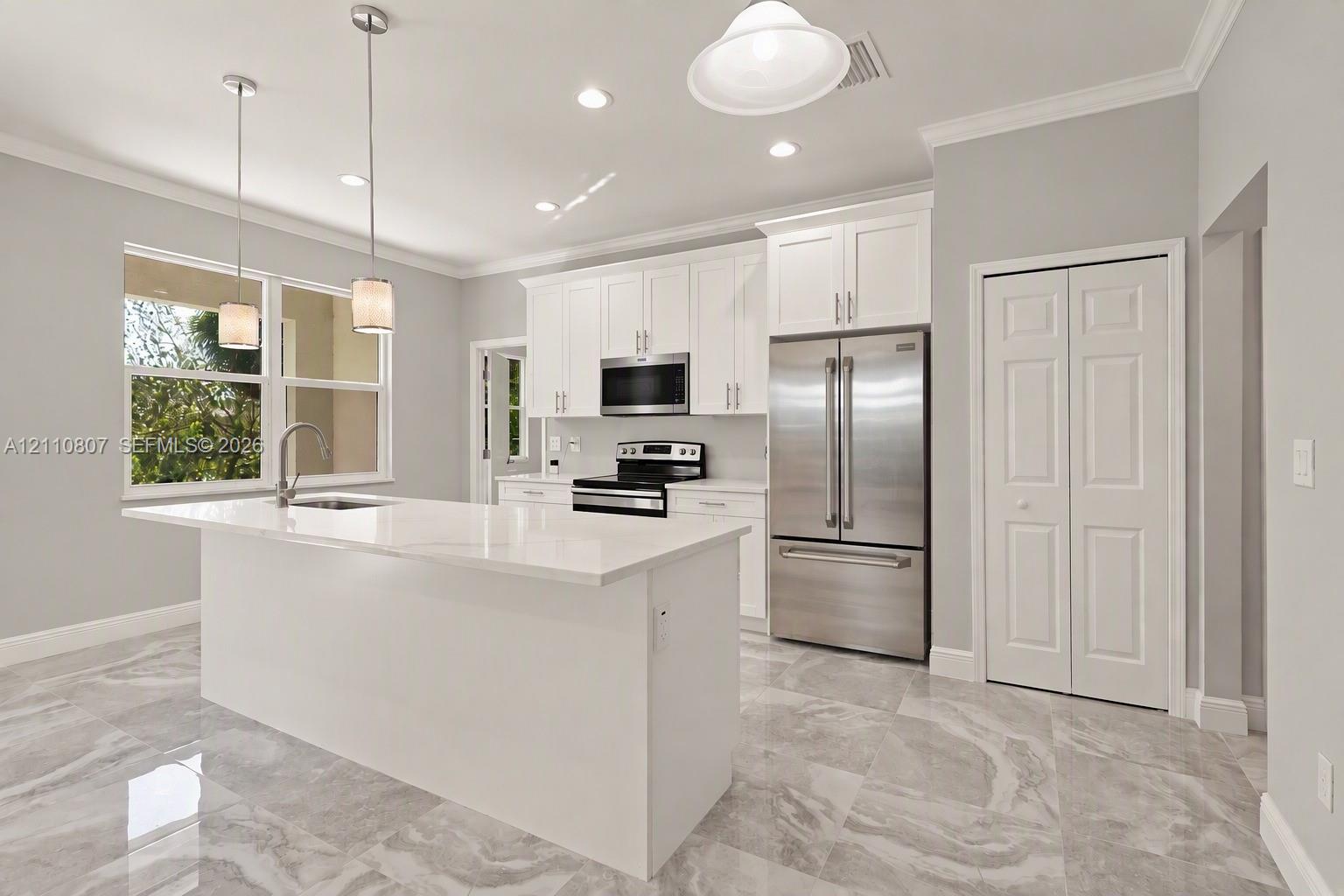 Kitchen featuring white cabinetry, stone-finish countertops, stainless steel appliances, a central island with an integrated sink, and polished light-toned tile flooring