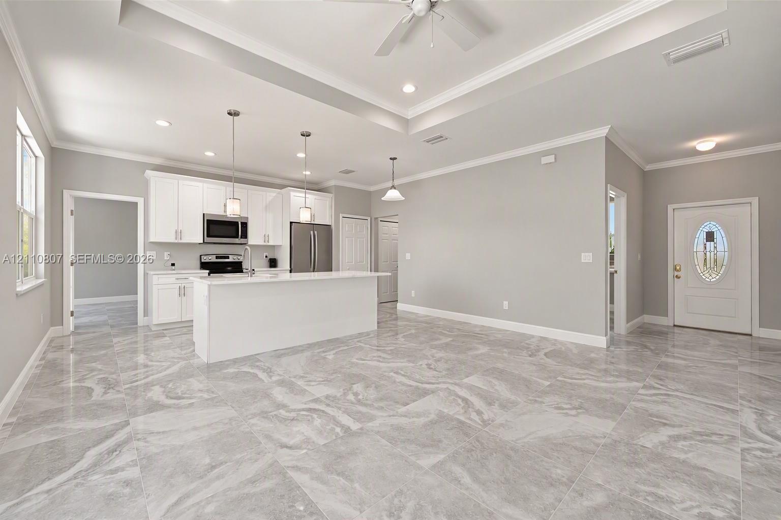 Open-concept space featuring oversized tile flooring, recessed lighting, tray ceilings with crown molding, white cabinetry, and a kitchen island