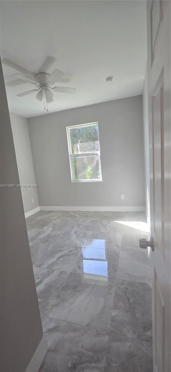 Polished stone-finish flooring, neutral wall tones, single-pane window, and white ceiling fan with integrated lighting