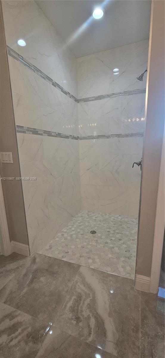 Walk-in shower featuring large-format stone-patterned wall tile, a horizontal mosaic tile accent band, a pebble-stone floor, and wall-mounted plumbing fixtures