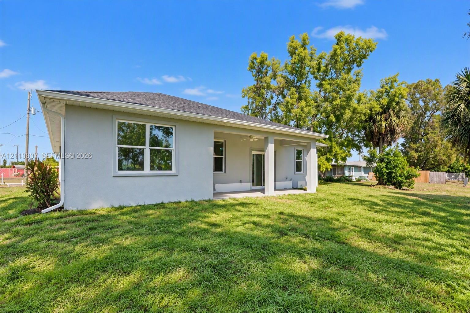 Exterior featuring a stucco facade, covered rear porch with a ceiling fan, and a spacious grass yard