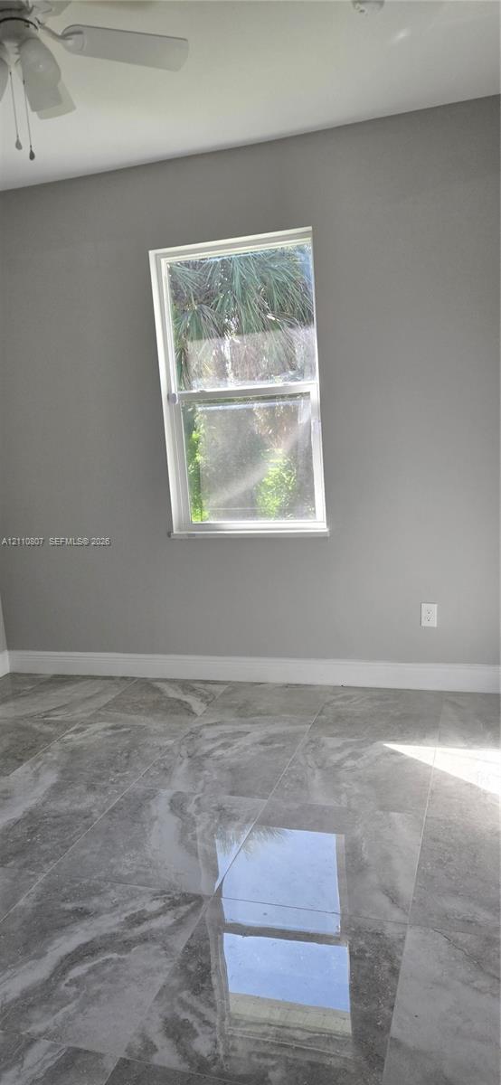 Neutral-toned interior featuring large-format polished tile flooring, white-framed window, and a ceiling-mounted fan