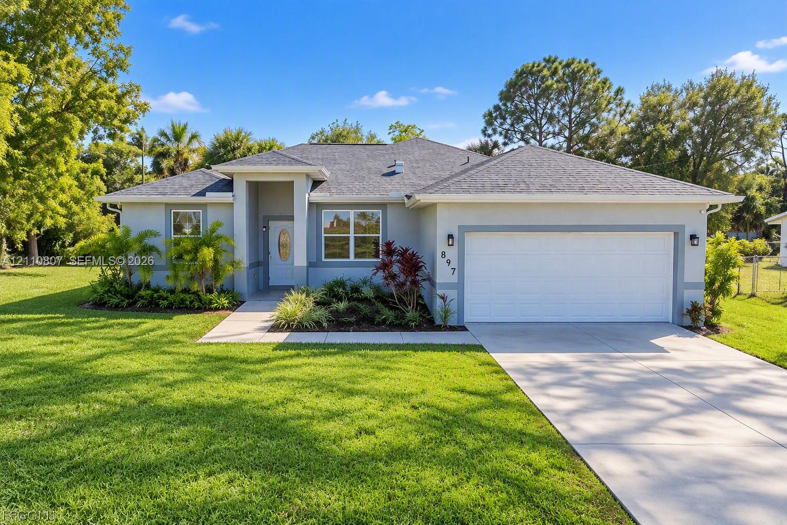 Single-story residence featuring a light-toned stucco exterior, hip roof, two-car garage, concrete driveway, and landscaped front yard