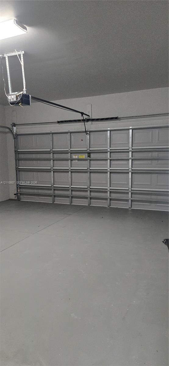 Two-car garage featuring a sectional overhead door, automated garage door opener, finished concrete flooring, and interior lighting