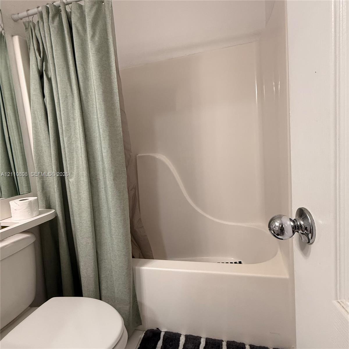 Integrated white acrylic tub and wall surround featuring a chrome-finish door knob