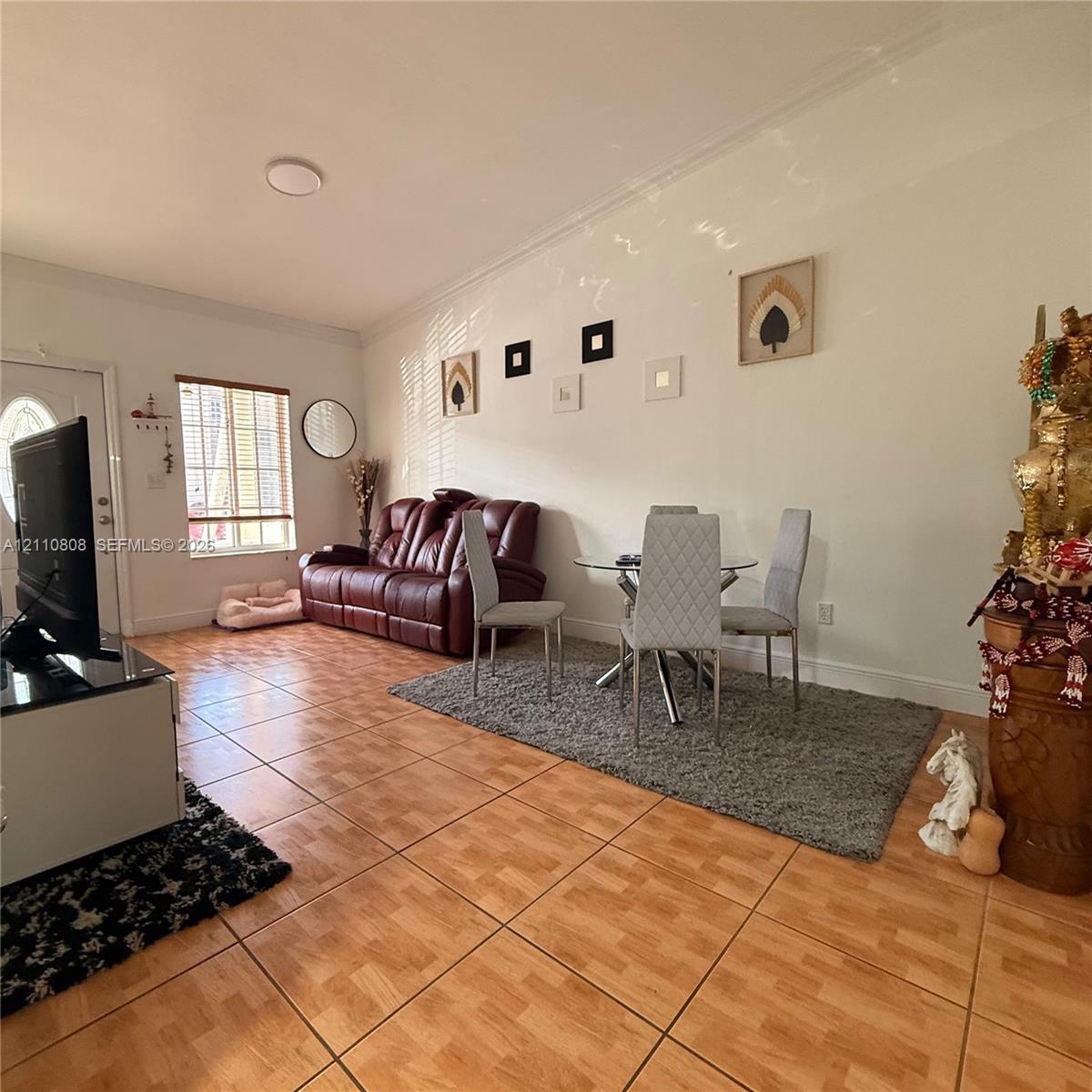 Living area featuring wood-finish tile flooring, crown molding, and a multi-pane window