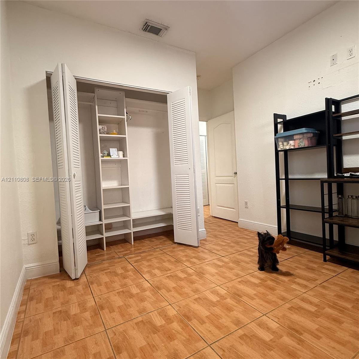 Room featuring wood-finish tile flooring, a built-in closet with louvered bifold doors, and integrated floor-to-ceiling shelving