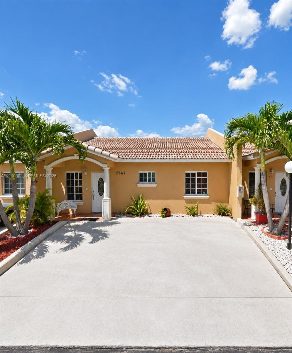 Stucco exterior featuring a clay tile roof, arched entryway with decorative columns, and a concrete driveway Stucco exterior featuring a clay tile roof, arched entryway with decorative columns, and a concrete driveway