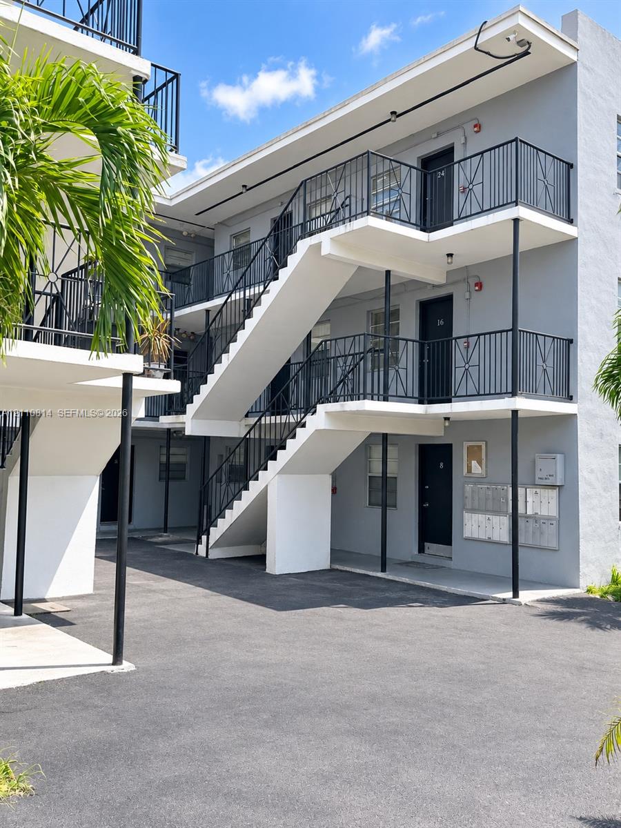 Multi-story exterior featuring a gray stucco facade, black metal staircases, decorative balcony railings, and exterior mailboxes