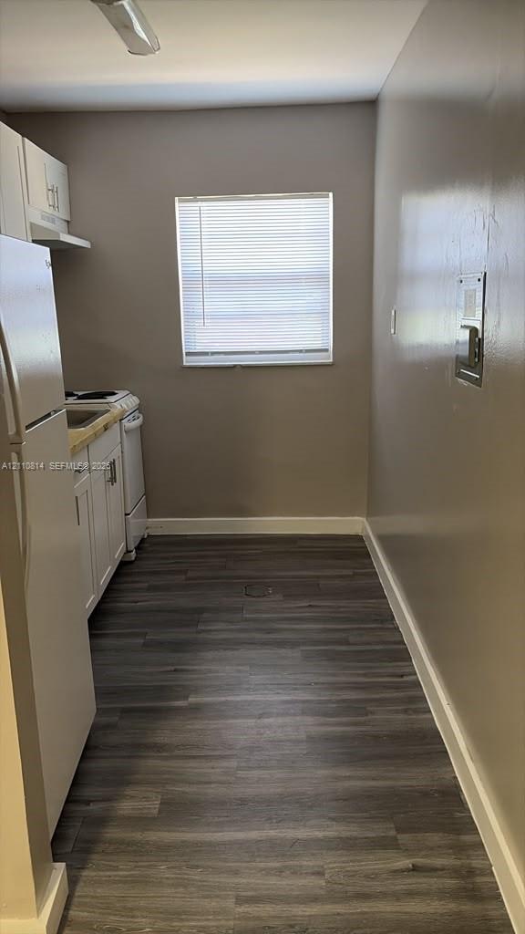 Kitchen featuring wood-finish flooring, white cabinetry, a built-in electric range, and a refrigerator
