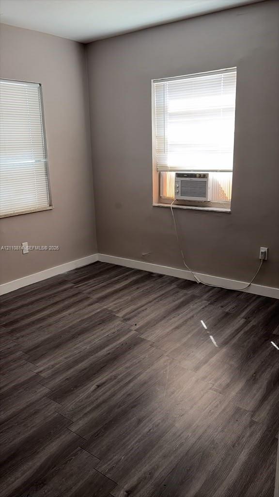Neutral-toned room featuring wood-finish flooring, two windows with horizontal blinds, and a wall-mounted air conditioning unit