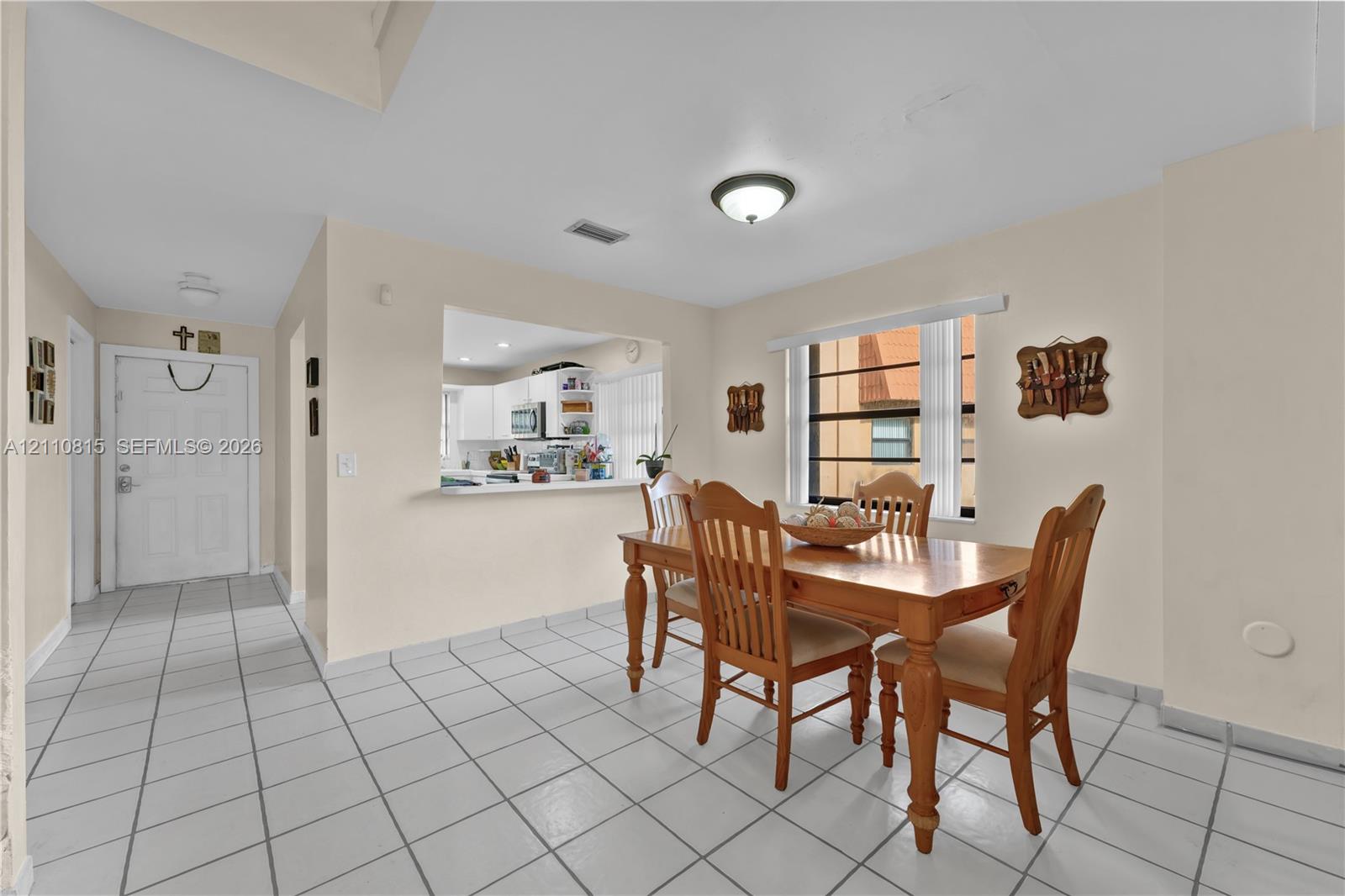 Interior space featuring large-format tile flooring, a pass-through window to the kitchen, and a window with horizontal blinds