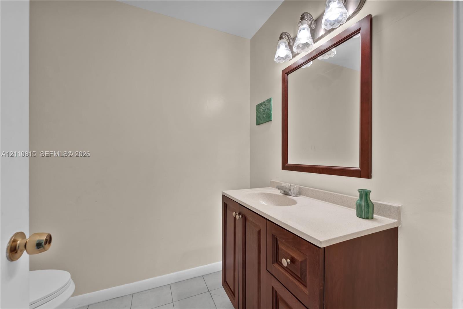 Bathroom featuring a wood-finish vanity with a stone-surface countertop, an integrated sink, a framed mirror, and a three-bulb light fixture