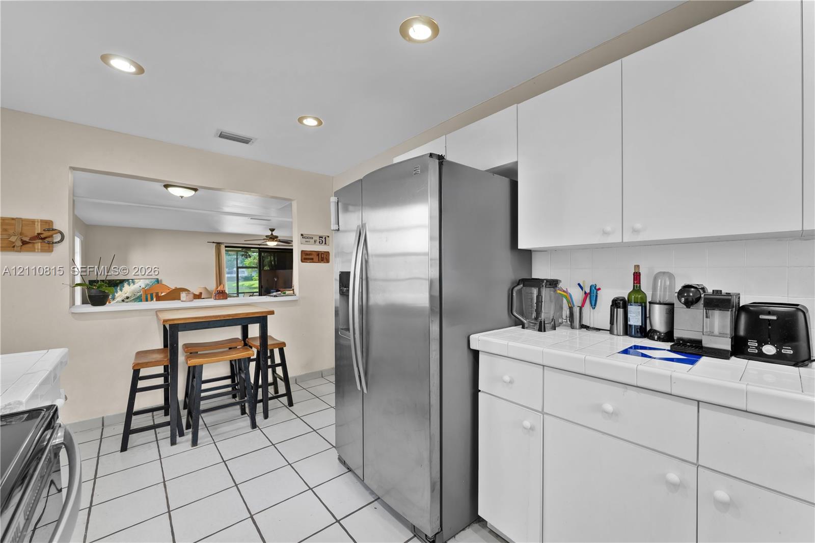 Kitchen featuring white cabinetry, ceramic tile countertops, stainless steel side-by-side refrigerator, ceramic tile flooring, and recessed ceiling lighting