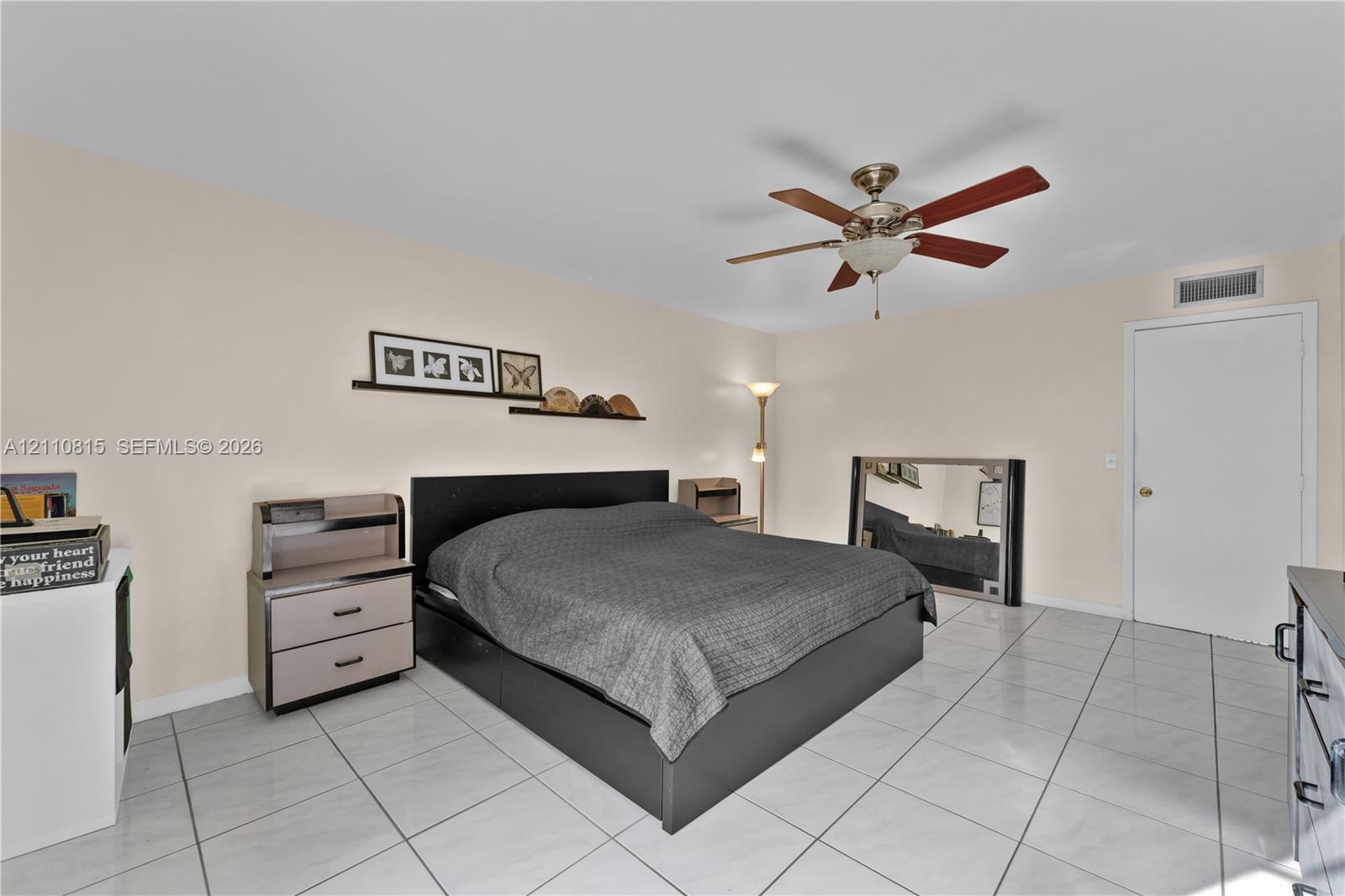 Neutral-toned room featuring large-format ceramic tile flooring, a centered ceiling fan with integrated lighting, and a white interior door