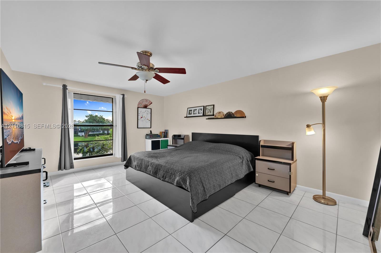 Neutral tile flooring, ceiling fan with light fixture, and large window