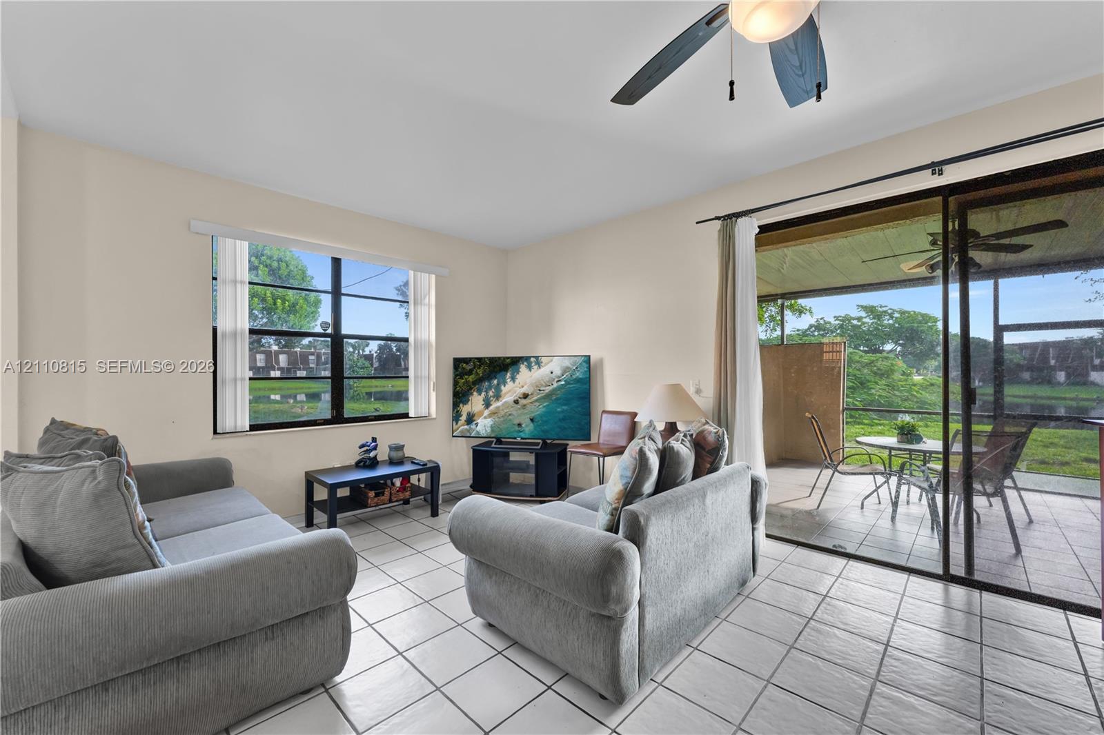 Living area featuring tile flooring, ceiling fan, large window, and sliding glass doors opening to a screened lanai