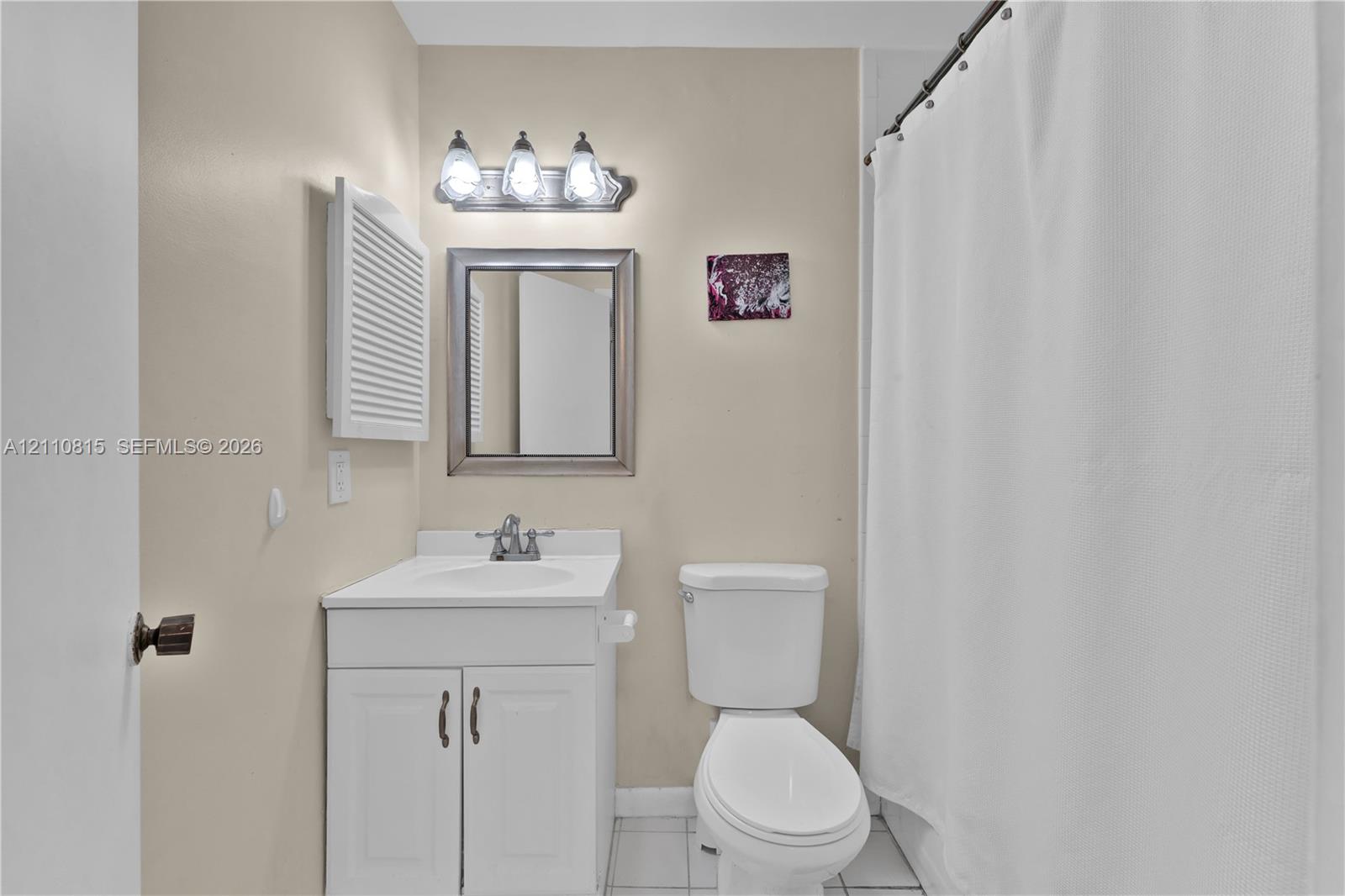 Bathroom featuring a white vanity cabinet with a stone-top integrated sink, a framed wall mirror, a three-light vanity fixture, and tiled flooring
