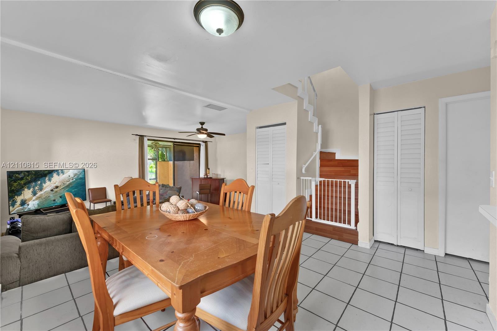 Interior area featuring white tile flooring, staircase with wood-finish treads, ceiling fan with light fixture, and dual-closet storage with louvered doors