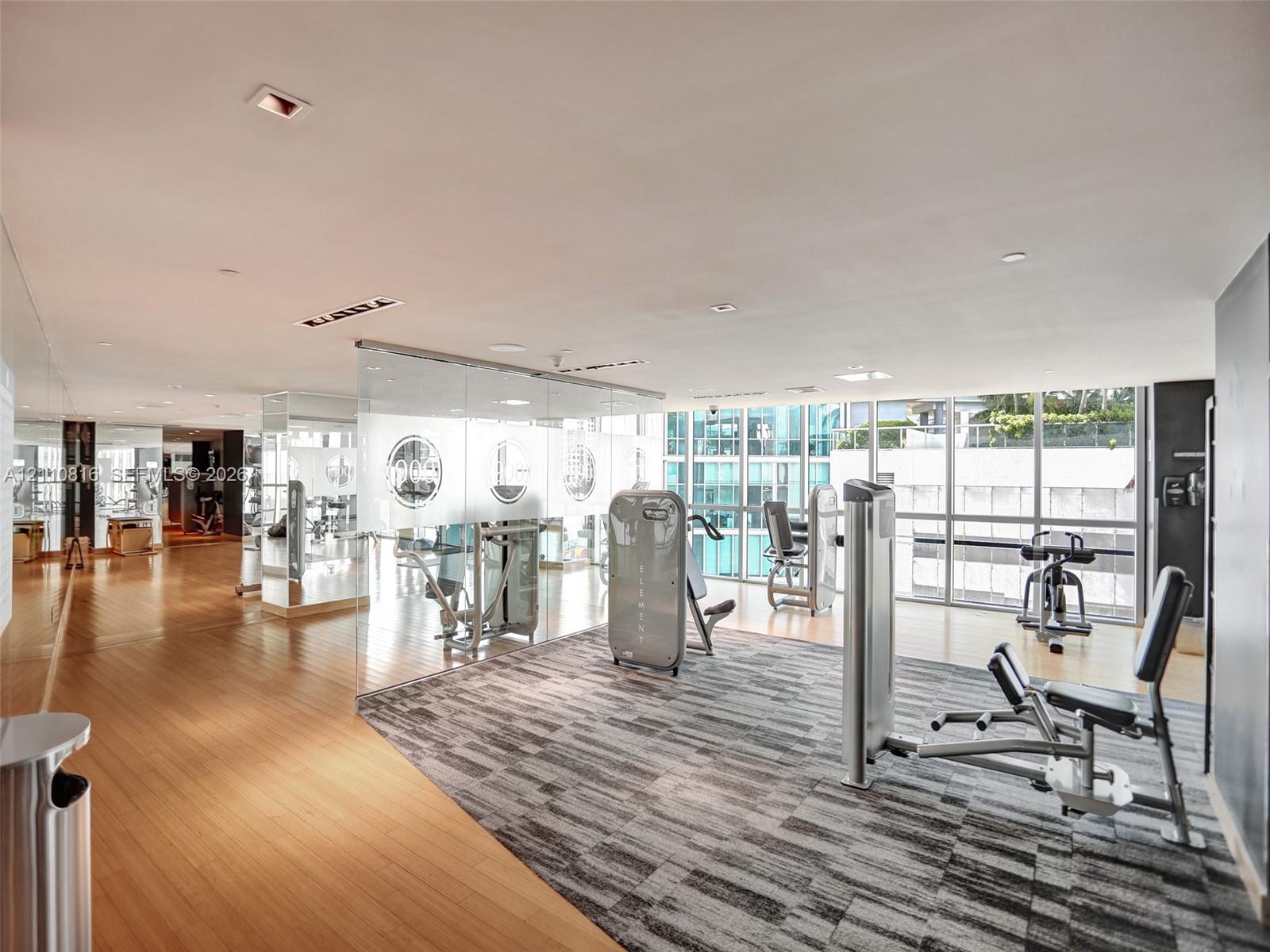 Fitness facility featuring wood-finish flooring, floor-to-ceiling glass wall panels, expansive windows, recessed lighting, and wall-to-wall mirrors