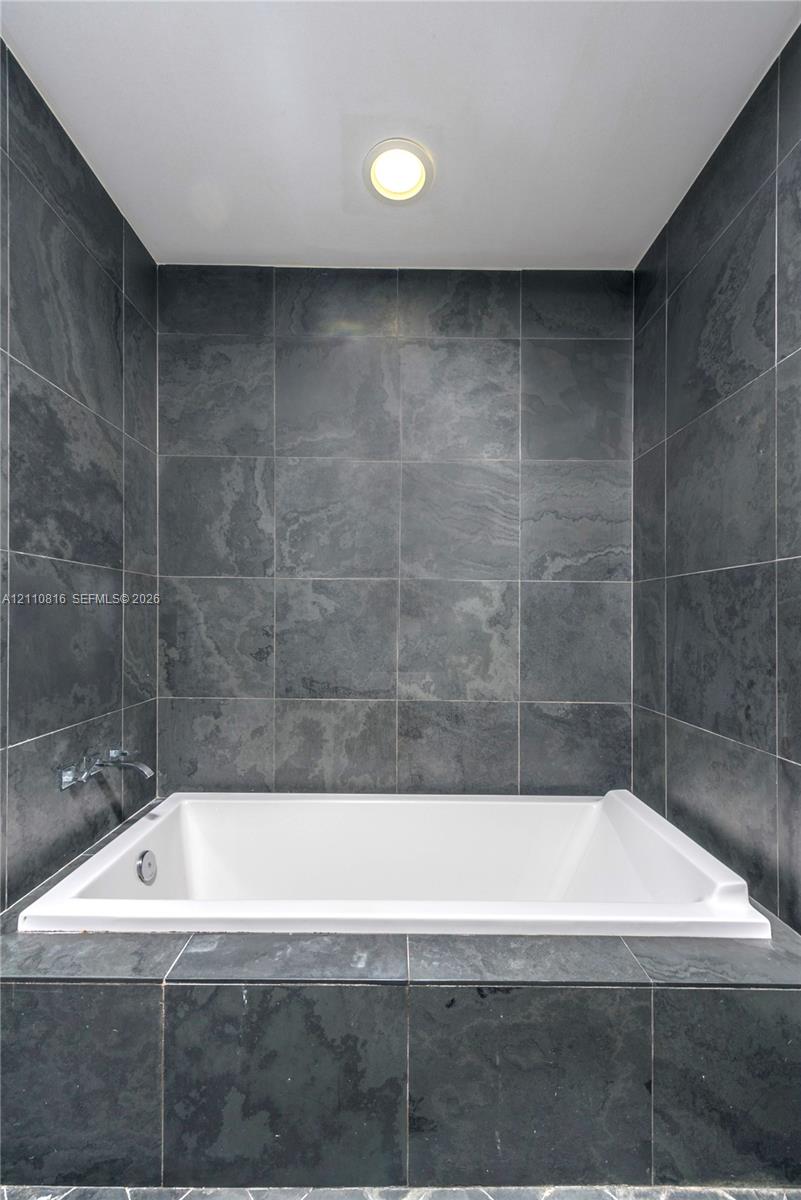 Built-in soaking tub featuring a white acrylic finish, surrounded by charcoal-toned stone tile surround and matching full-height tiled wall accents with integrated chrome faucet hardware