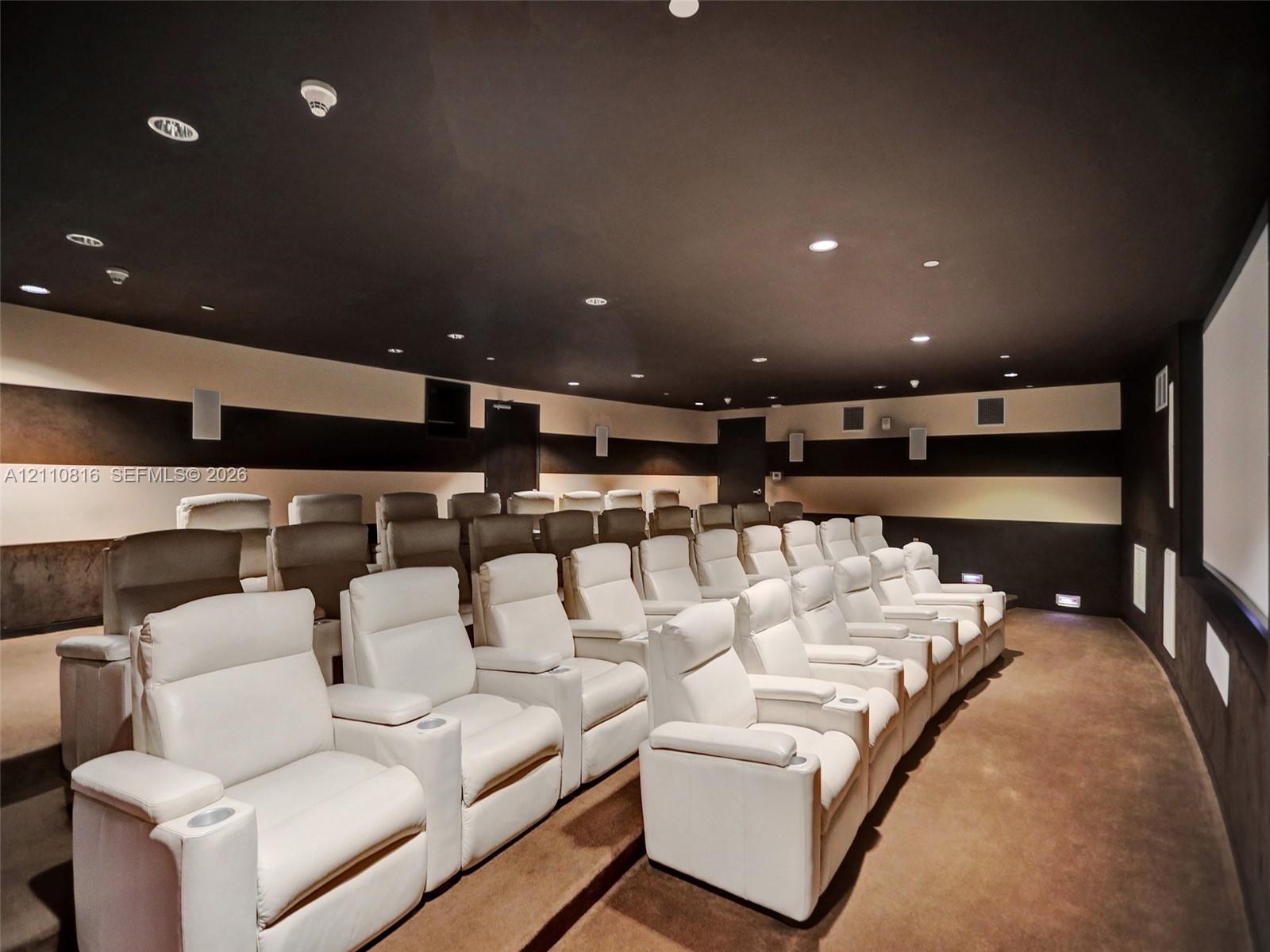 Dedicated media room featuring tiered platform flooring, integrated ceiling recessed lighting, wall-mounted speakers, and large-format projection screen