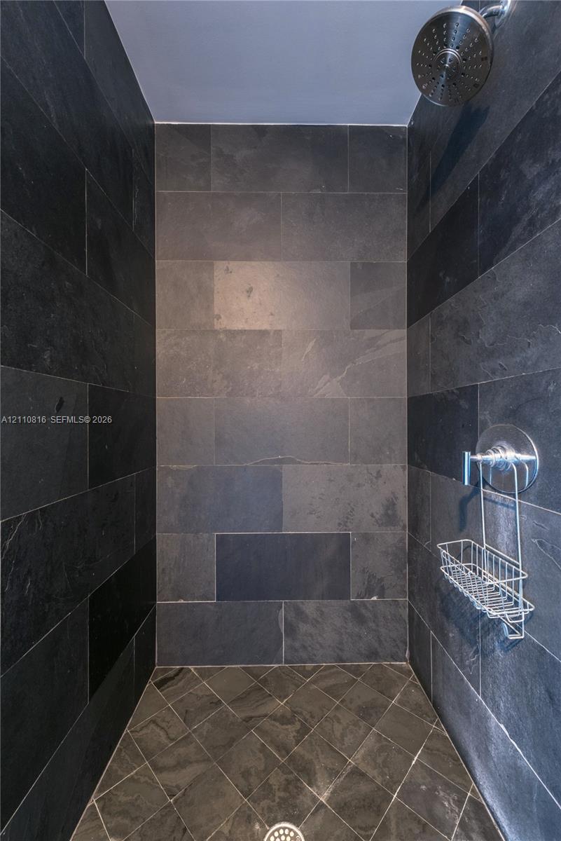 Walk-in shower enclosure featuring full-height charcoal stone tile walls, coordinating diamond-patterned tile flooring, a circular chrome showerhead, and a matching chrome pressure-balance valve