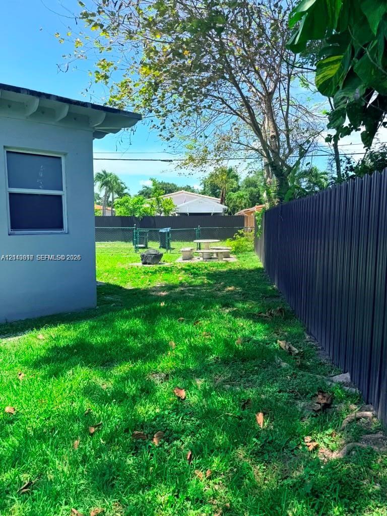 Backyard featuring a grass lawn, metal privacy fencing, and mature trees