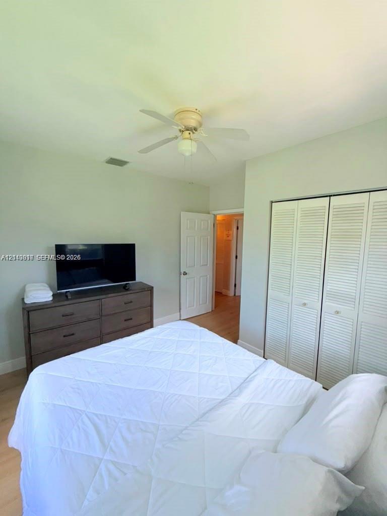 Room featuring wood-finish flooring, a ceiling fan, and louvered closet doors