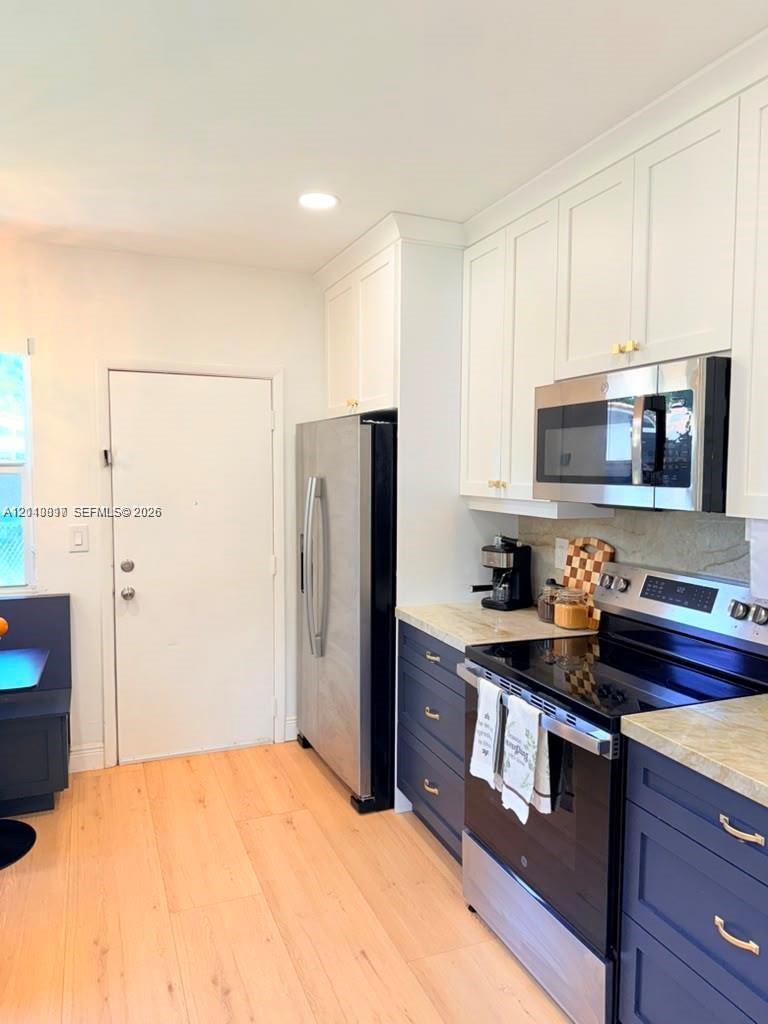 Kitchen featuring two-tone shaker-style cabinetry, wood-finish flooring, stone-surfaced countertops, and stainless steel appliances